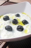 === Ingredience ===
1 velká salátová okurka
1 velký bílý jogurt (vyberte si nějaký hustší, třeba Holandia, nebo kdo má možnost si koupit originál řecký bílý jogurt)
2 lžičky koření tzaziky od "Avokádo"
1 stroužek česneku
černé olivy na ozdobu
olivový olej

=== Příprava ===
Okurku si nastrouhejte na hrubém struhadle. Posypte ji kořením tzaziky, promíchejte a nechte odpočívat cca 15 miut.

Zkoušela jsem i koření tzaziky od Vitany nebo Knoru, ale nebylo to vůbec dobré. Takže pátrejte po koření tzaziky od Avokáda. Nebo si namíchejte svoje: kromě soli je tam sušený česnek, cibule a kopr.

Okurku si přendejte do sítka nebo cedníku a vymačkejte z ní přebytečnou vodu. Vraťte zpět do misky, přidejte bílý jogurt a prolisovaný česnek a 1 lžíci olivového oleje. Vše dobře promíchejte. Případně podle chuti přidejte ještě trošku koření tzaziky.

Pokud máte čerstvé bylinky, přidejte si tam trošku čersvého kopru nebo máty.

Servírujte do mističek s černými olivami a pár kapkami olivového oleje. Výborný je k tomu arabský nebo řecký chléb.

Dobrou chuť.